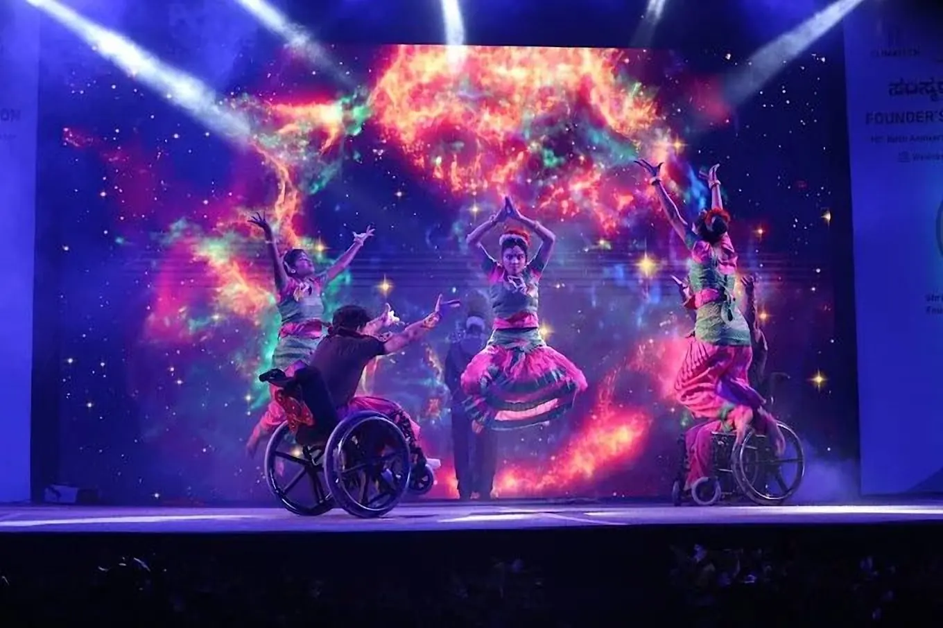 Inclusive dance performance on stage against a cosmic LED wall with beam lights